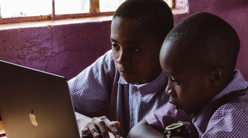 Two young boys in school uniforms focus on a laptop, studying together indoors.