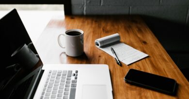 A tidy workspace featuring a laptop, coffee cup, phone, and notepad on a wooden desk.