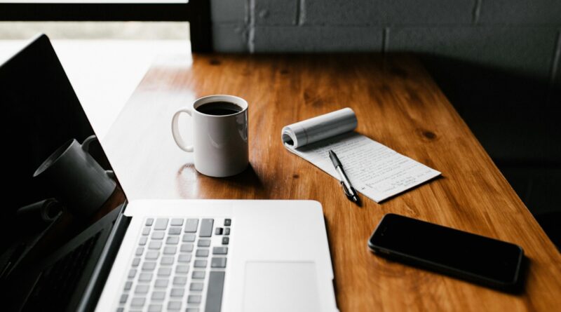 A tidy workspace featuring a laptop, coffee cup, phone, and notepad on a wooden desk.