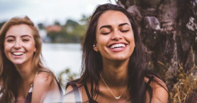 Two women happily laughing together outdoors by a serene lakeside.